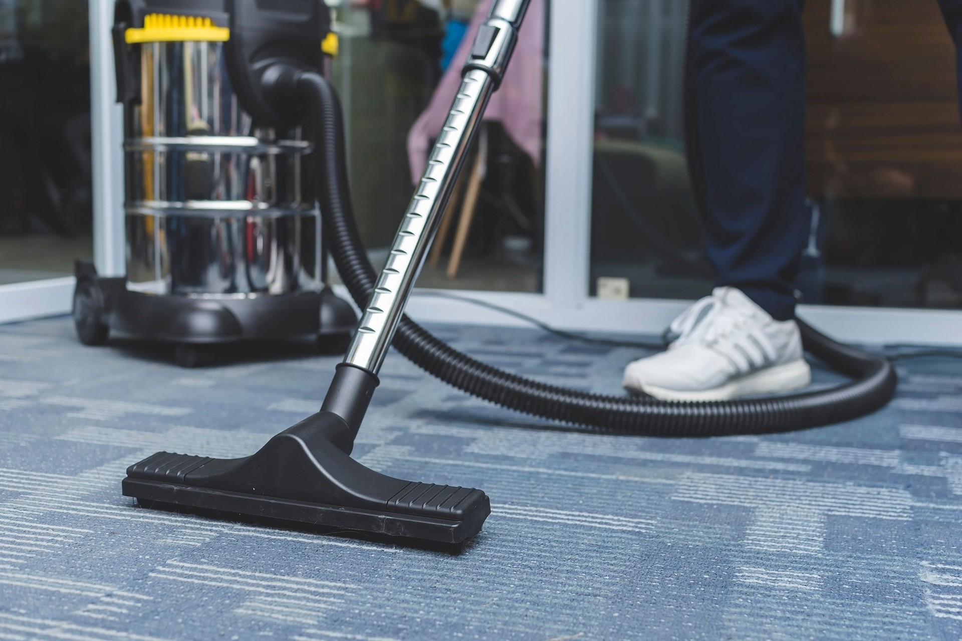 A york pa man cleans the carpet flooring of an office with an upright vacuum cleaner with an attached upholstery nozzle.